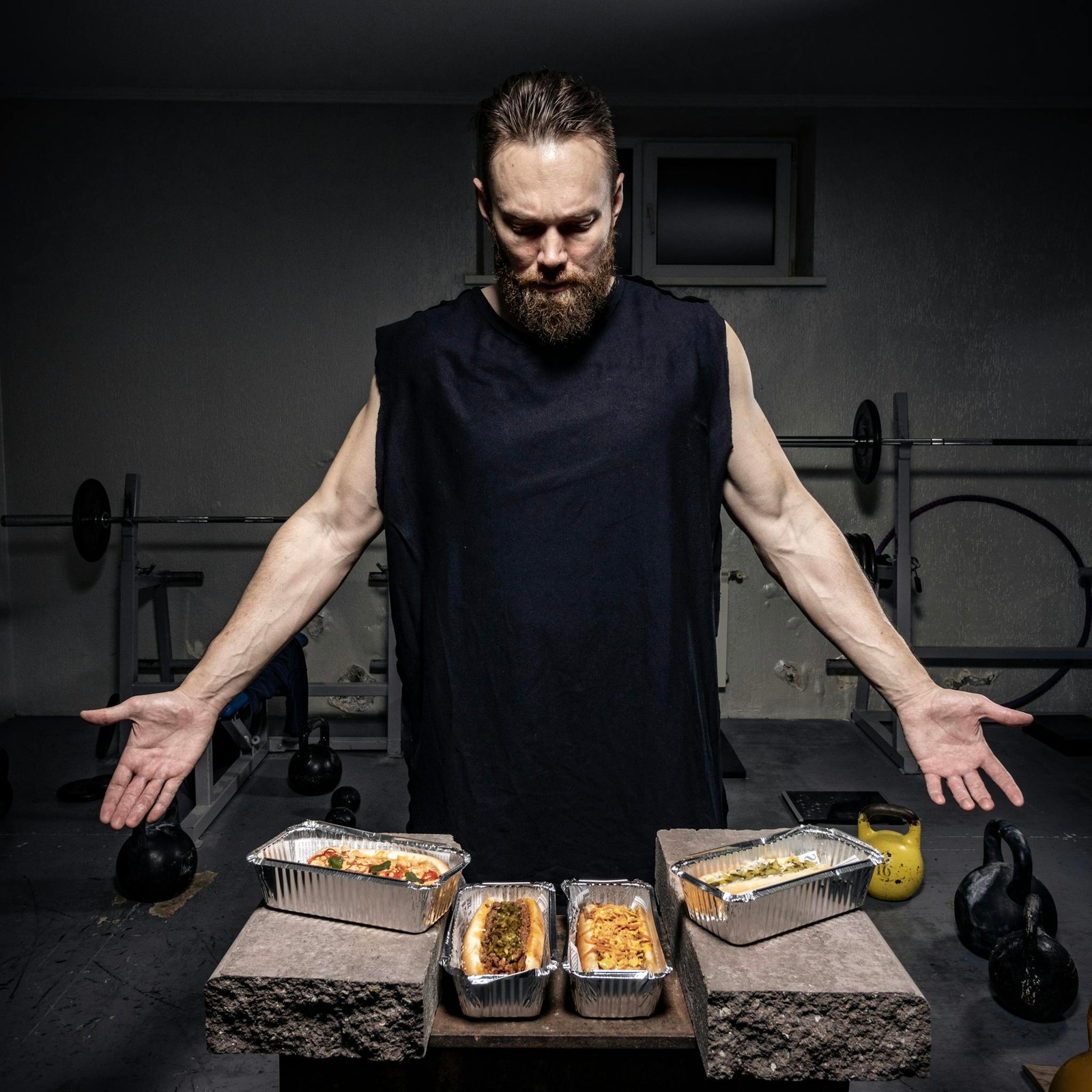A bearded man in a gym presents nutritious meals in aluminum pans.